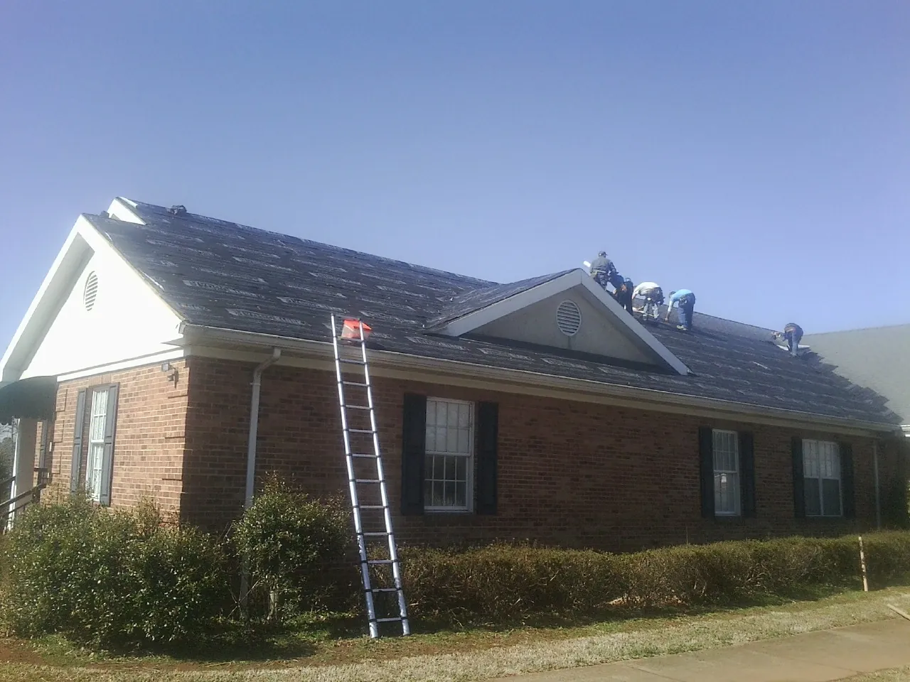 Crew tearing shingles off a brick ranch roof with a ladder set — Emergency Roof Repair work by our crew in Cascade